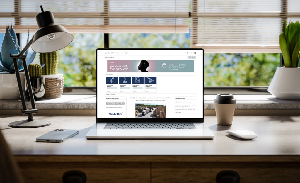 A laptop with a Totara LMS screen from BSW sits on on a stylish wooden desk within a loft-style interior, with green spaces in the background visible through the window - 3d render
